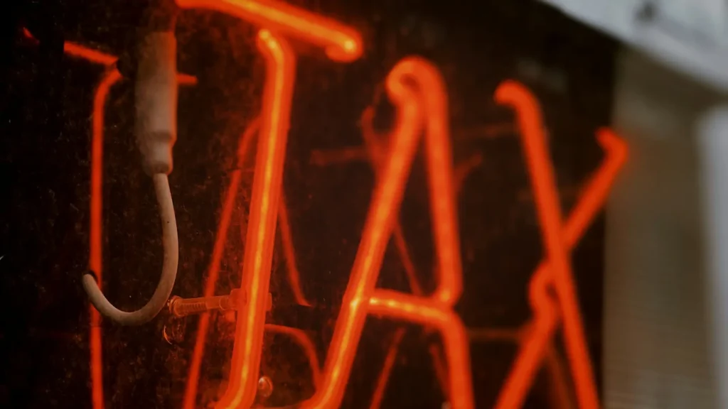 A glowing neon Tax sign against the reflection of a glass window.